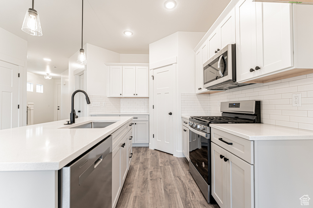 Kitchen with stainless steel appliances, light wood-type flooring, light countertops, white cabinetry, and decorative backsplash