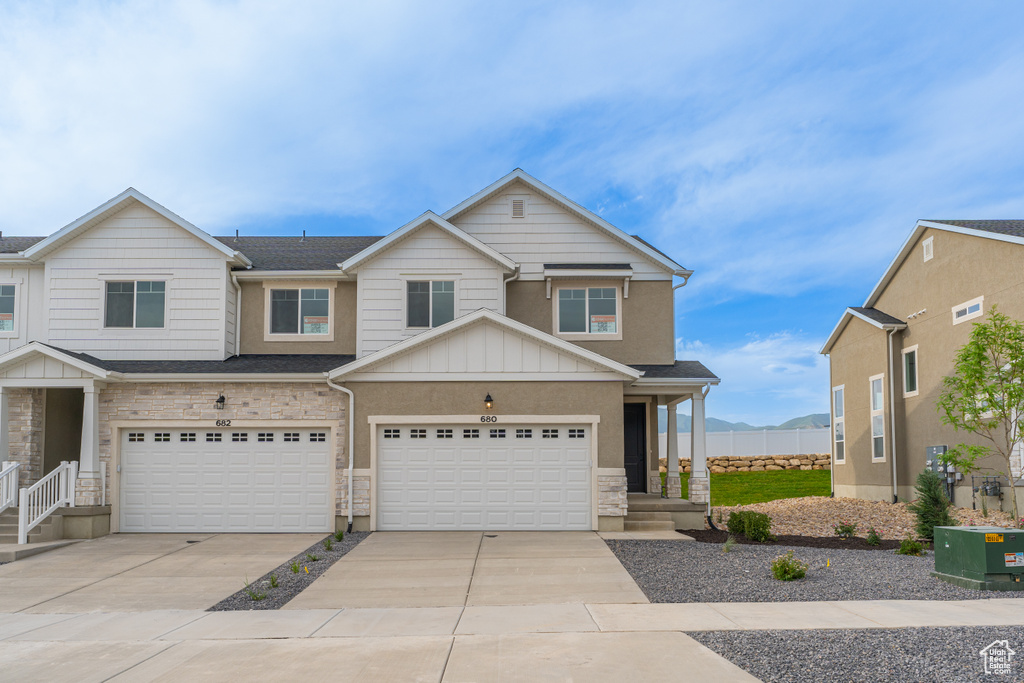 View of property featuring board and batten siding, concrete driveway, stone siding, and a garage