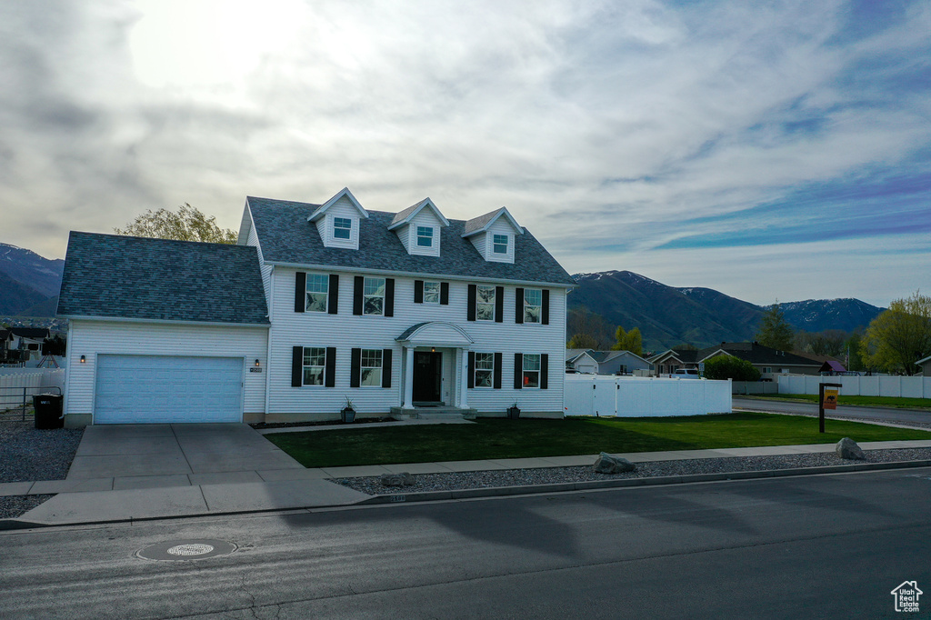 Colonial-style house with fence, a mountain view, an attached garage, and a front lawn