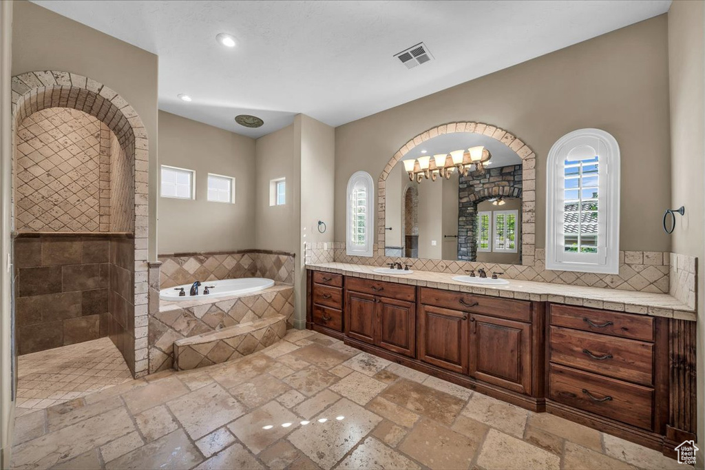 Bathroom featuring plenty of natural light, a bath, stone tile floors, double vanity, and recessed lighting