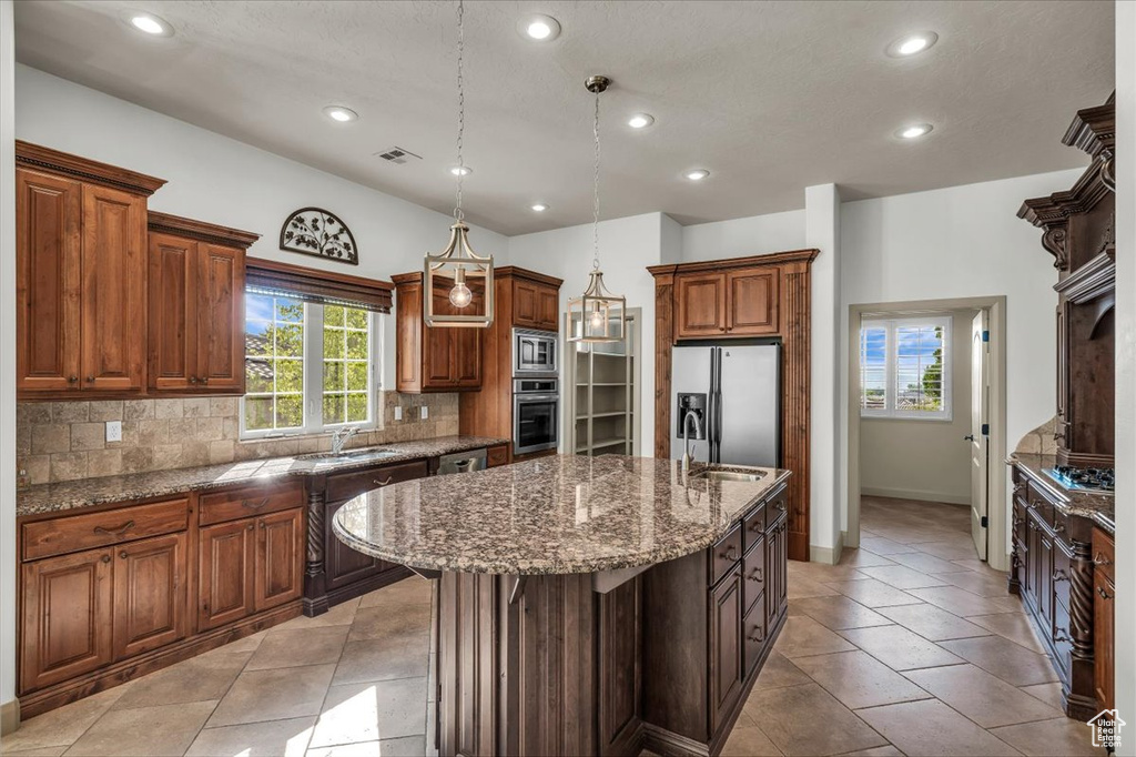 Kitchen with appliances with stainless steel finishes, tasteful backsplash, recessed lighting, a center island with sink, and dark stone counters
