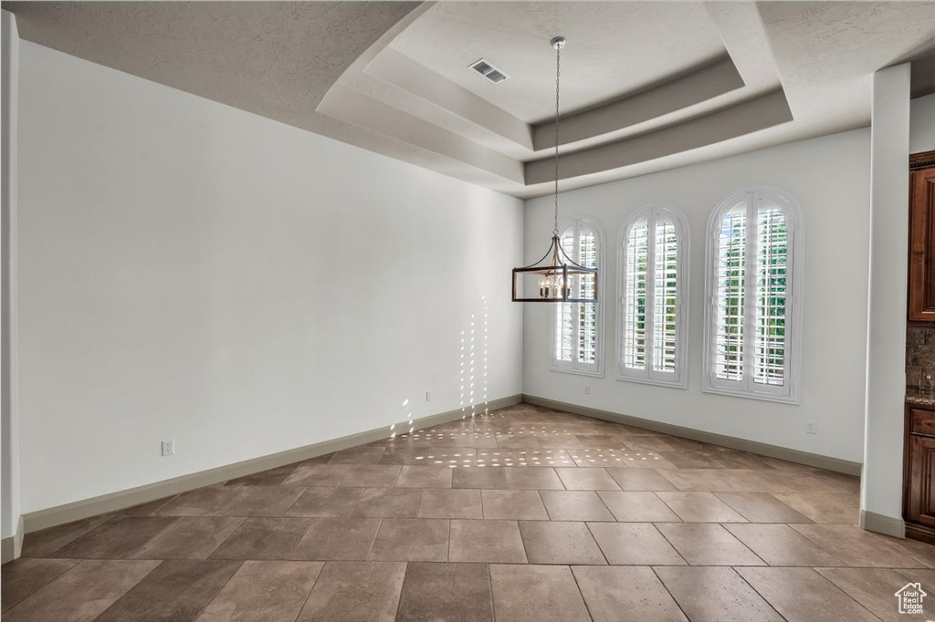 Empty room featuring a raised ceiling and a chandelier