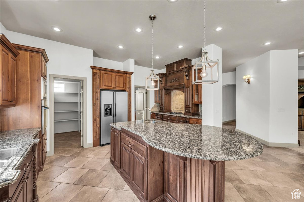 Kitchen with stainless steel appliances, an island with sink, stone counters, hanging light fixtures, and recessed lighting