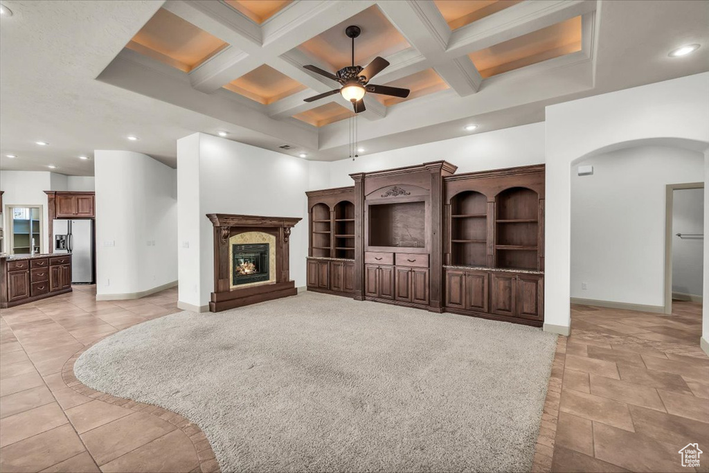 Unfurnished living room with coffered ceiling, arched walkways, a high ceiling, a ceiling fan, and beam ceiling