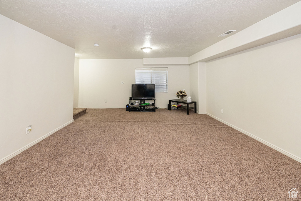 Unfurnished living room with a textured ceiling, carpet, visible vents, and baseboards