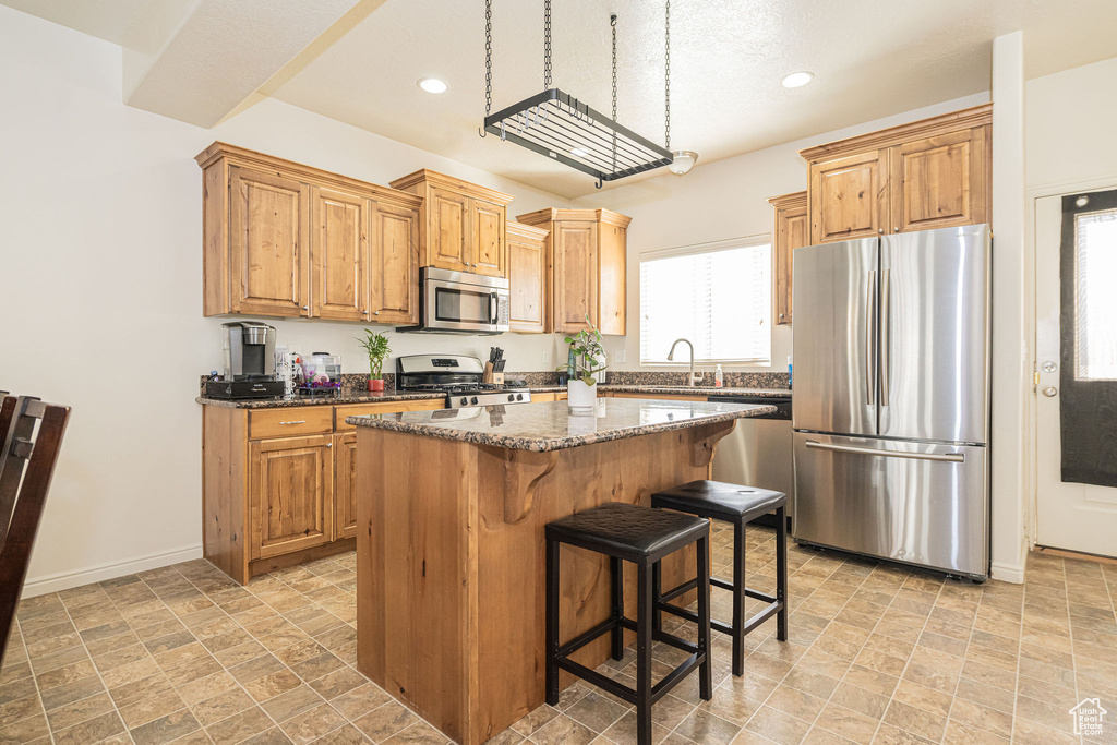 Kitchen with a center island, appliances with stainless steel finishes, a kitchen breakfast bar, dark stone countertops, and baseboards
