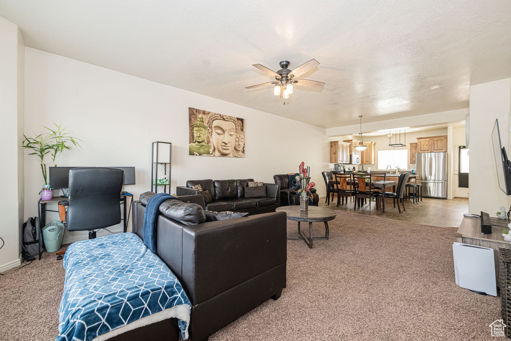 Living area with a textured ceiling, a ceiling fan, and light colored carpet