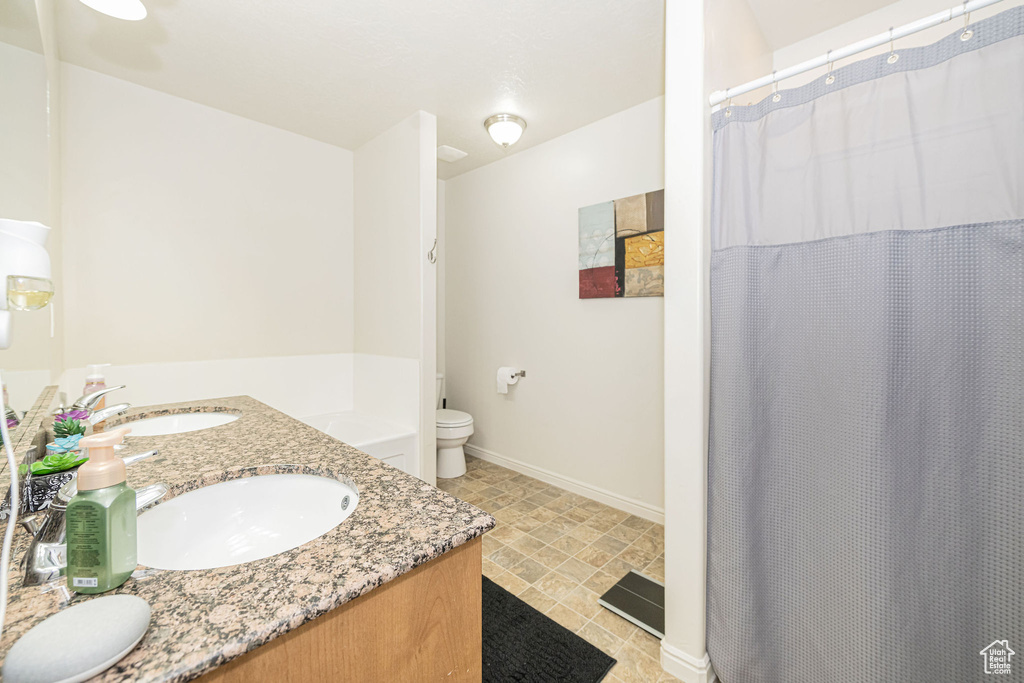 Bathroom featuring toilet, double vanity, baseboards, and a sink