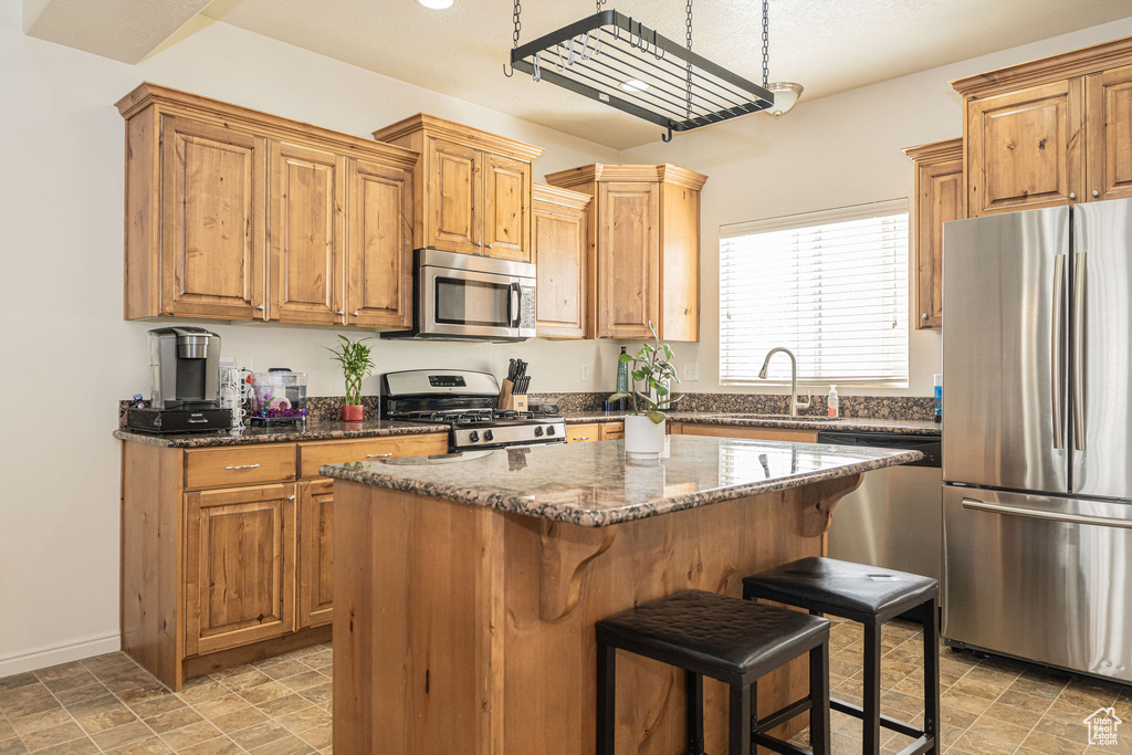Kitchen with a center island, a breakfast bar area, stainless steel appliances, a sink, and dark stone countertops