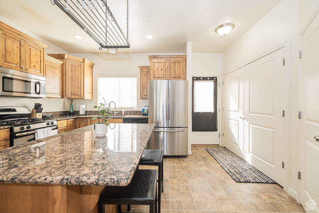 Kitchen with a breakfast bar, appliances with stainless steel finishes, a sink, a kitchen island, and dark stone counters