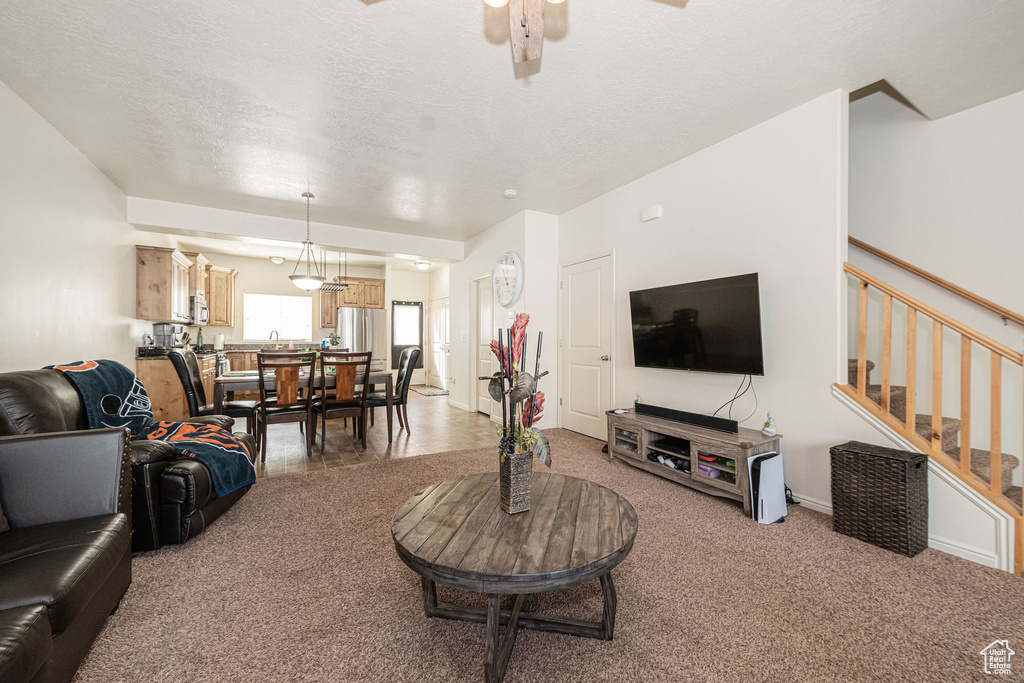 Carpeted living area with a textured ceiling, ceiling fan, and stairway