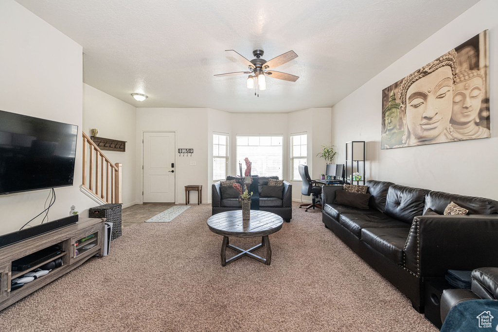 Living area with carpet flooring, ceiling fan, baseboards, and stairs