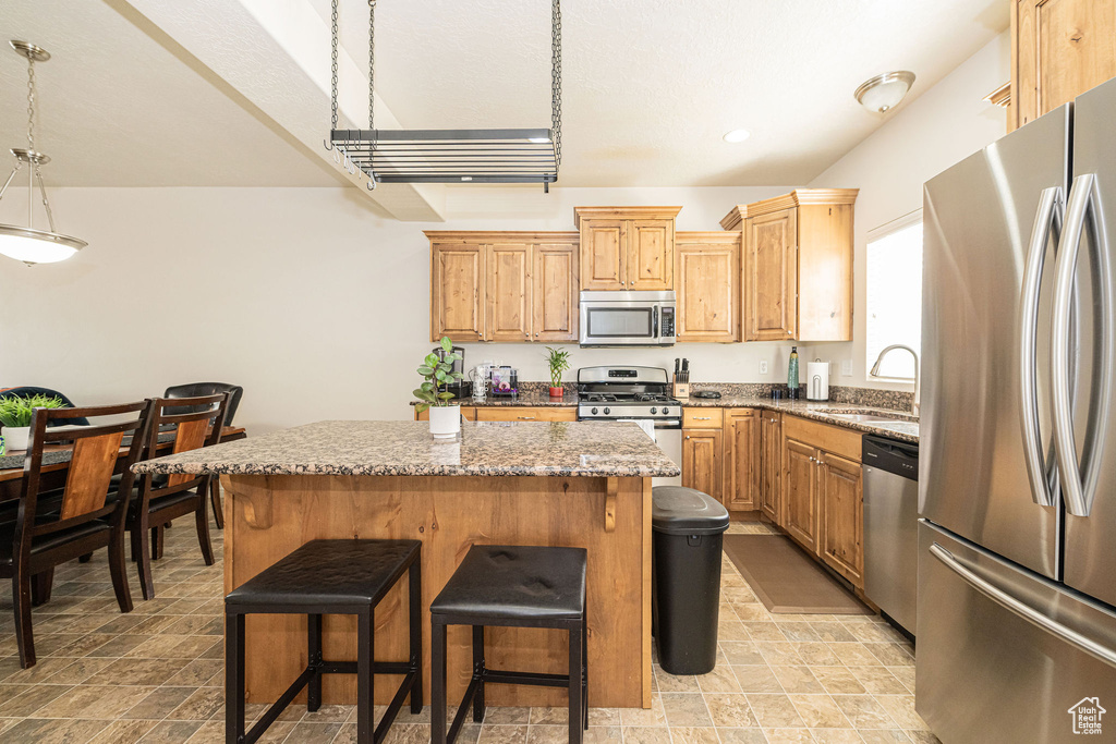 Kitchen with a kitchen island, appliances with stainless steel finishes, light stone countertops, a kitchen bar, and a sink