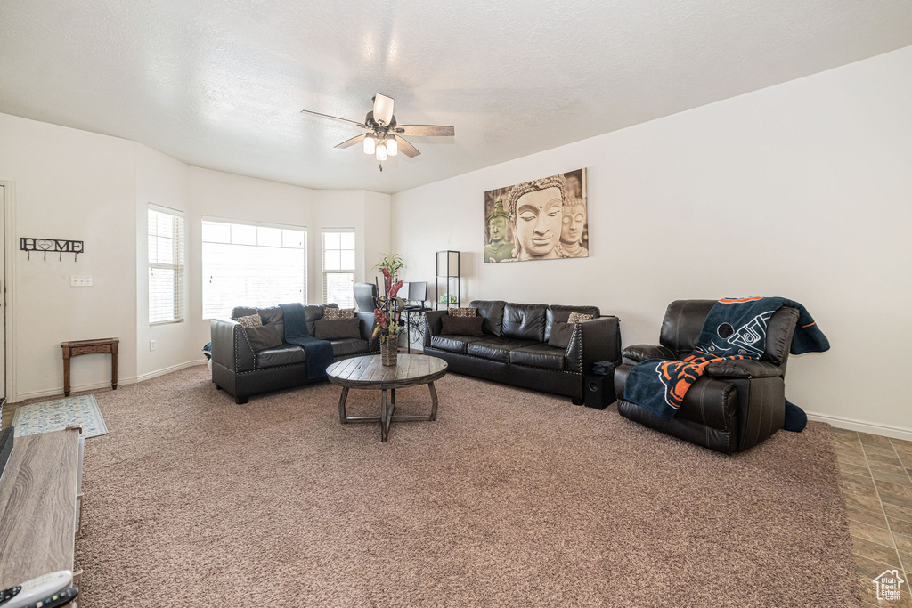Carpeted living room featuring a textured ceiling, a ceiling fan, and baseboards
