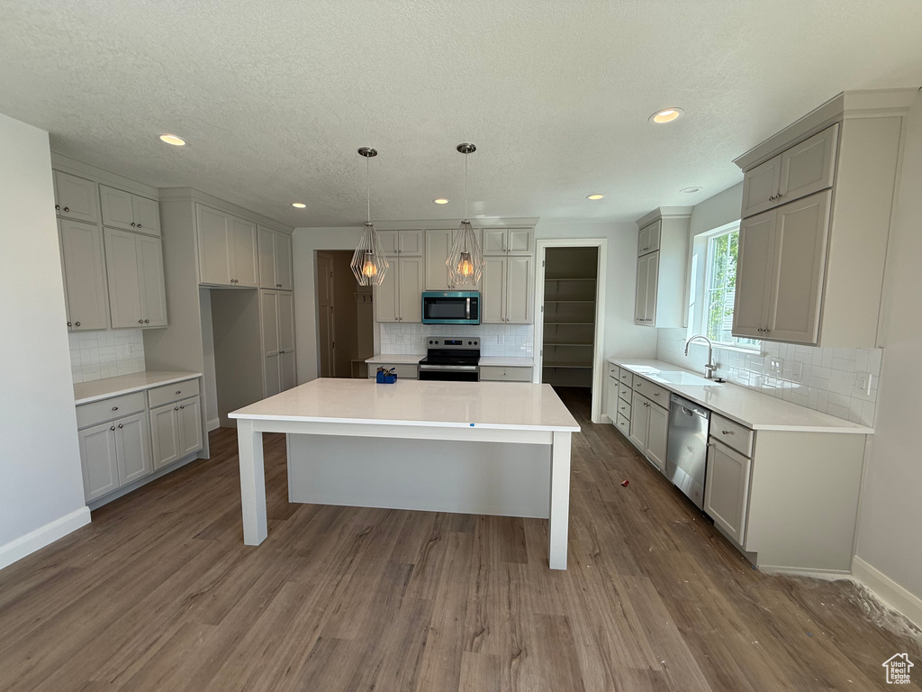 Kitchen featuring appliances with stainless steel finishes, a sink, backsplash, a center island, and dark wood finished floors