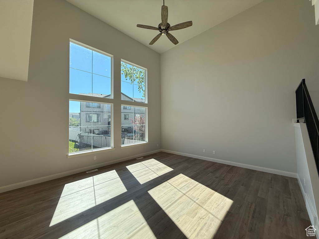 Spare room with high vaulted ceiling, dark wood-type flooring, baseboards, and ceiling fan