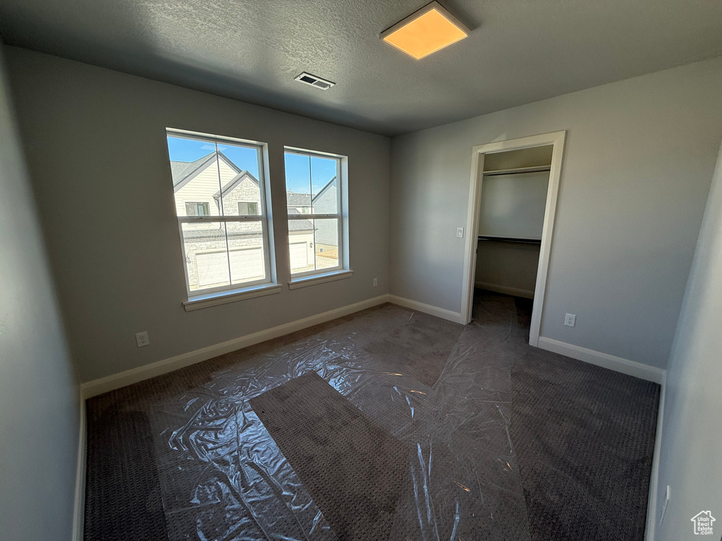 Unfurnished bedroom with carpet, baseboards, a spacious closet, and a textured ceiling