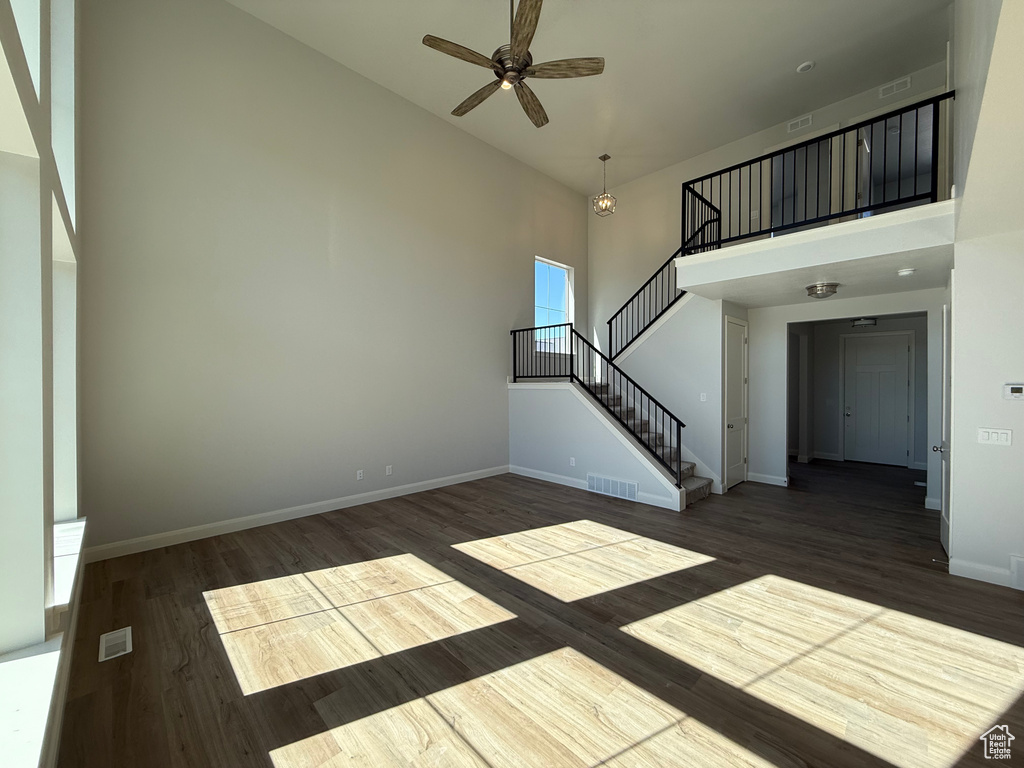 Unfurnished living room with a high ceiling, a ceiling fan, stairway, wood finished floors, and baseboards