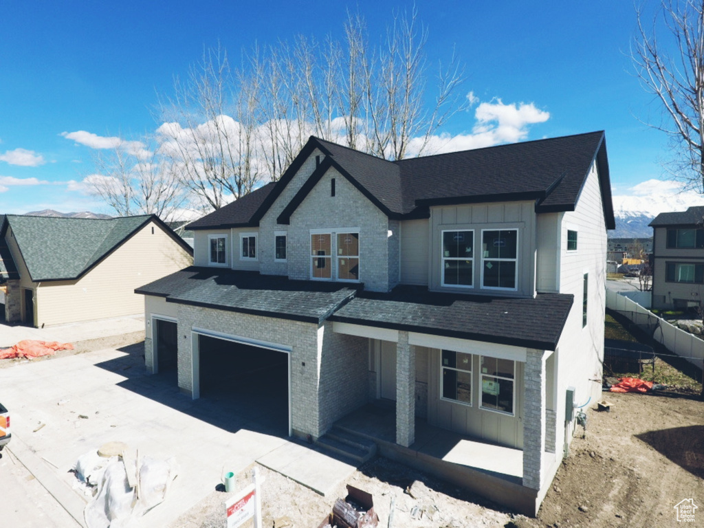 View of front of property featuring board and batten siding, driveway, a shingled roof, and fence
