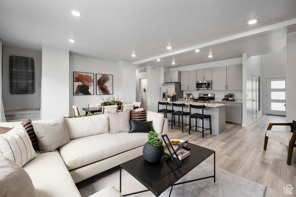 Living room with light wood-style flooring, visible vents, a textured ceiling, and recessed lighting