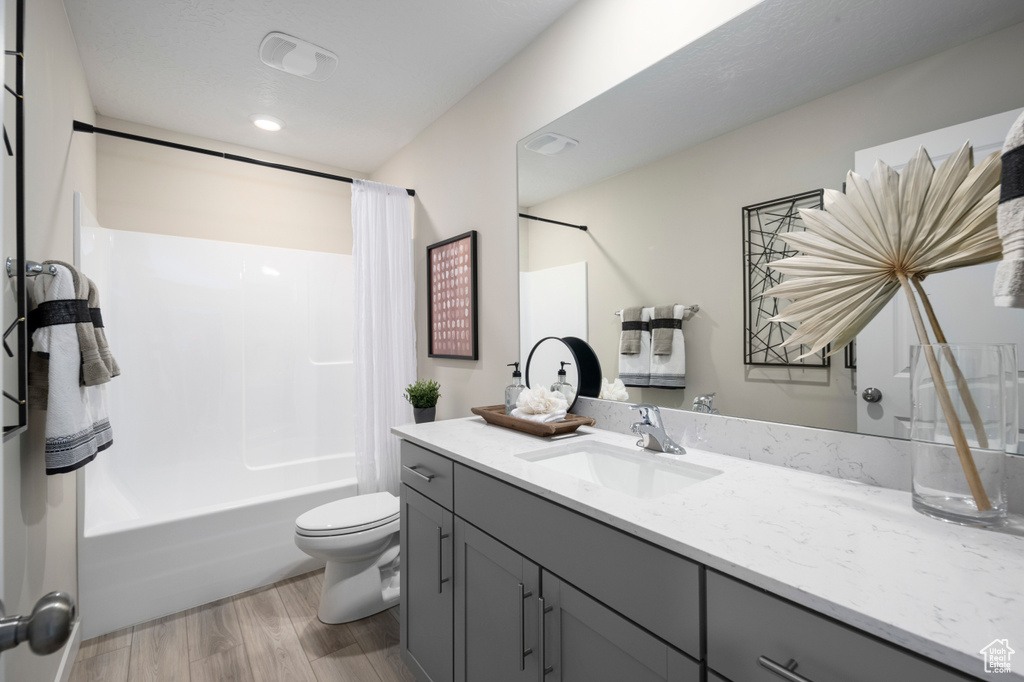 Bathroom with toilet, shower / tub combo, wood finished floors, and vanity