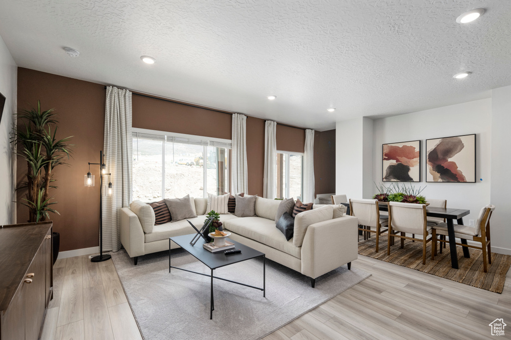 Living room featuring light wood-type flooring, a textured ceiling, baseboards, and recessed lighting
