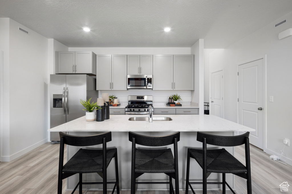 Kitchen featuring stainless steel appliances, a breakfast bar, a sink, and gray cabinetry