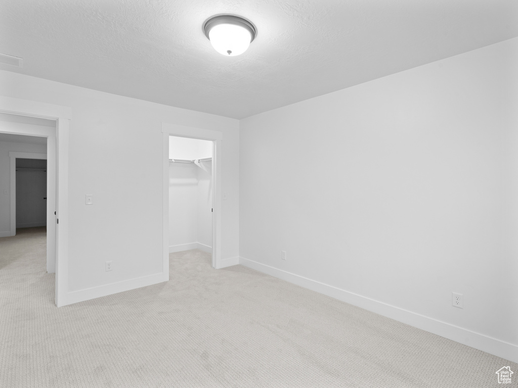 Unfurnished bedroom with light carpet, baseboards, a closet, and a walk in closet