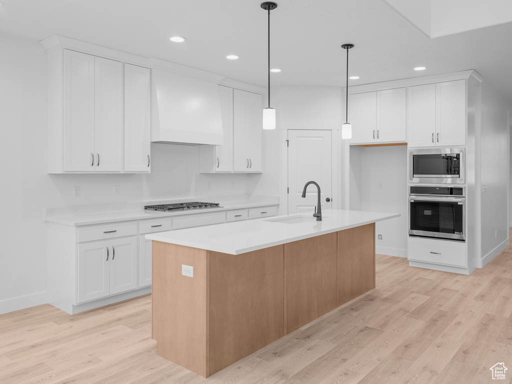 Kitchen featuring light wood finished floors, light countertops, custom range hood, white cabinets, and appliances with stainless steel finishes