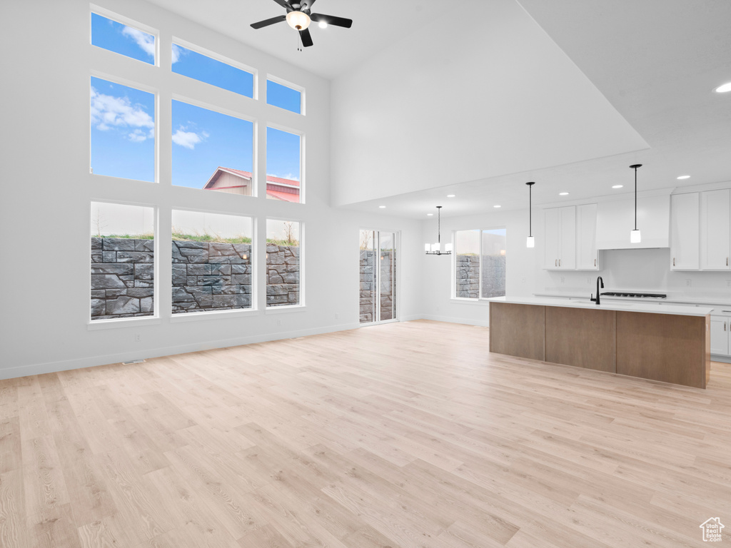 Unfurnished living room with ceiling fan with notable chandelier, baseboards, recessed lighting, and light wood finished floors