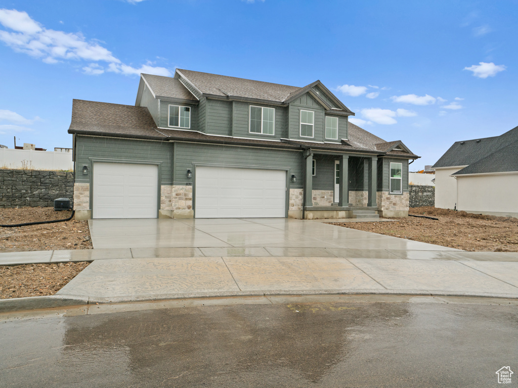 View of front of property featuring an attached garage, driveway, stone siding, and a shingled roof