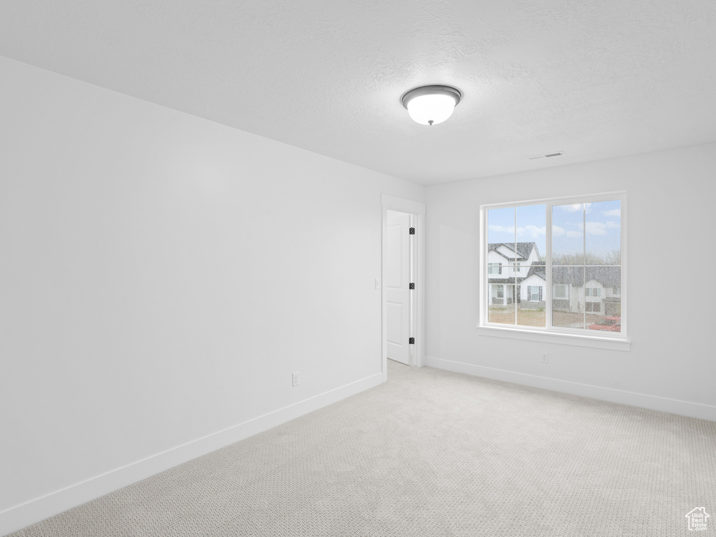 Spare room featuring baseboards, a textured ceiling, and light carpet