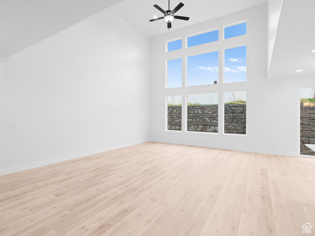 Unfurnished living room with light wood-type flooring, baseboards, high vaulted ceiling, and ceiling fan