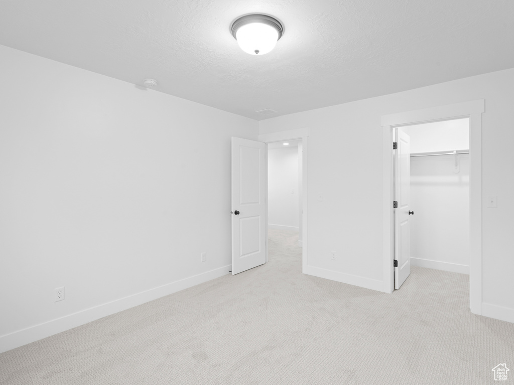Unfurnished bedroom with light carpet, a textured ceiling, baseboards, a spacious closet, and a closet