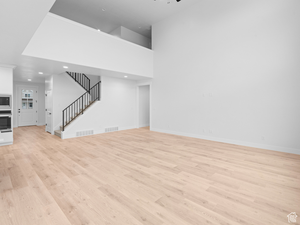 Unfurnished living room with stairway, visible vents, light wood finished floors, and baseboards