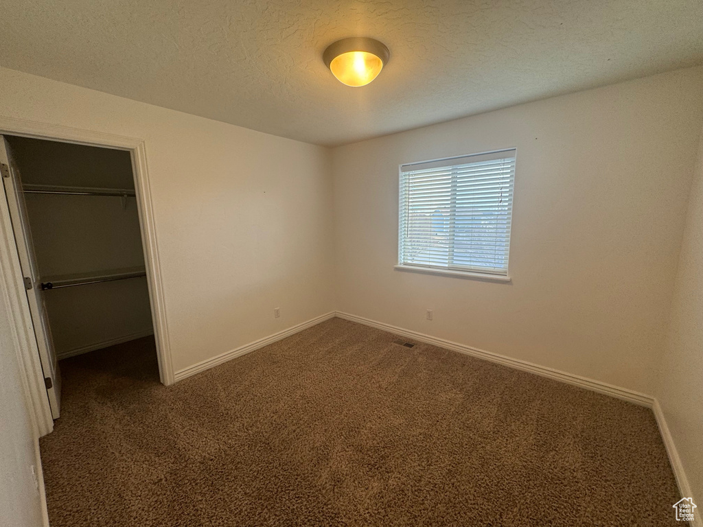 Unfurnished bedroom featuring baseboards, a walk in closet, dark colored carpet, a textured ceiling, and a closet