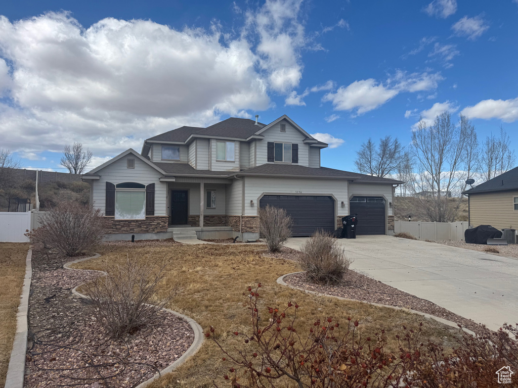 View of front of home with a garage, concrete driveway, stone siding, and fence