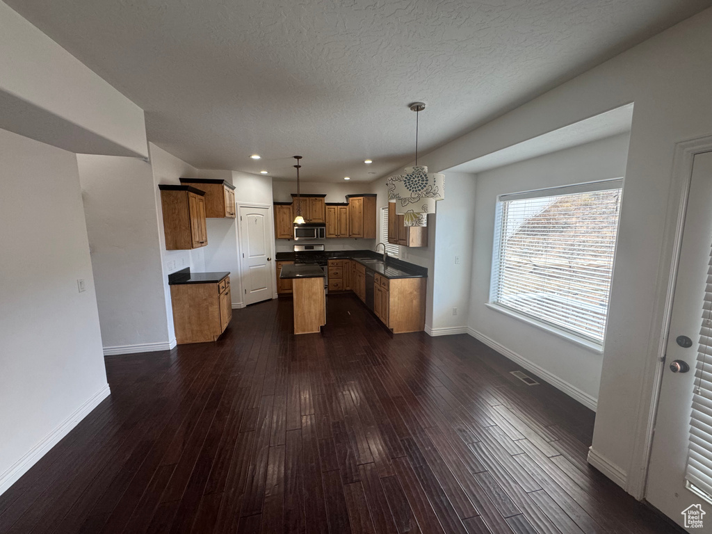 Kitchen featuring dark wood-style flooring, baseboards, appliances with stainless steel finishes, brown cabinets, and dark countertops