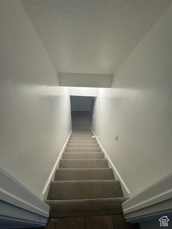 Stairs with lofted ceiling, carpet flooring, and a textured ceiling
