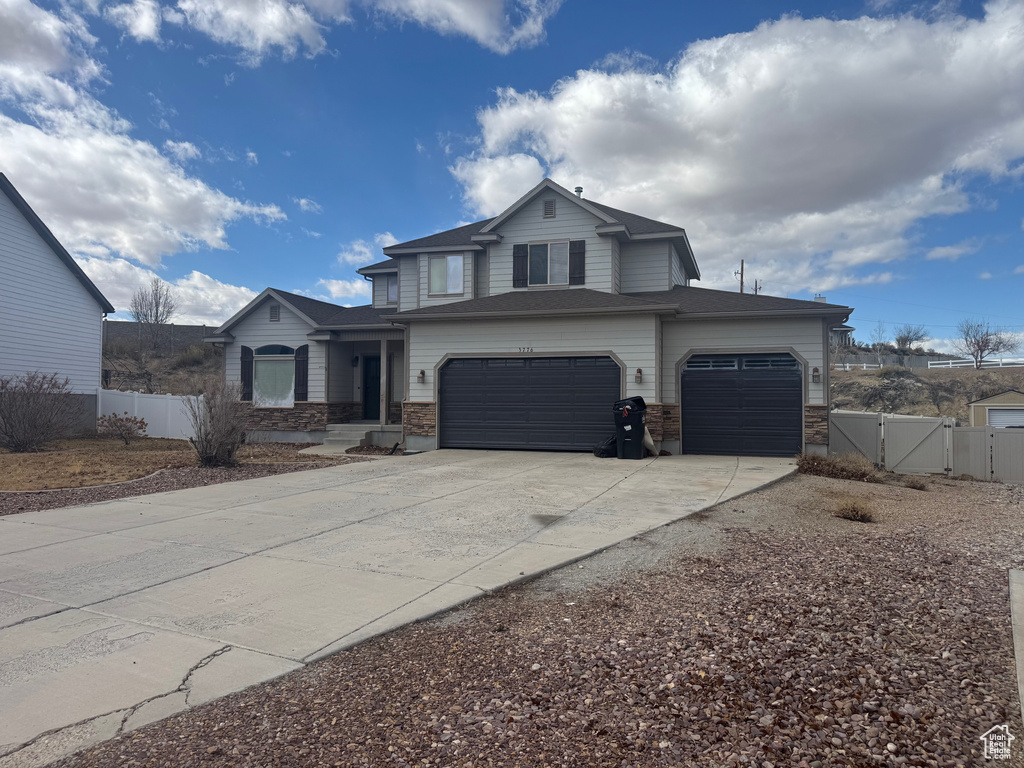 View of front of home with stone siding, a gate, fence, and concrete driveway