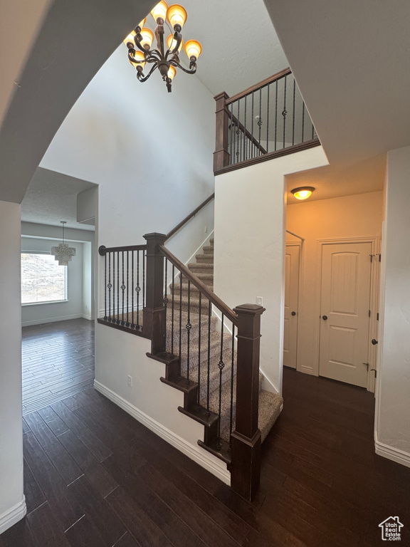 Staircase featuring baseboards, a high ceiling, wood finished floors, and an inviting chandelier