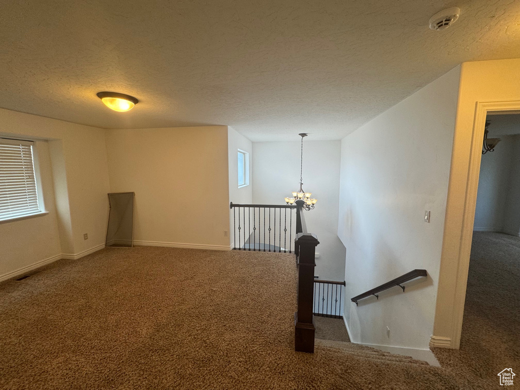 Carpeted spare room featuring a notable chandelier, baseboards, and a textured ceiling