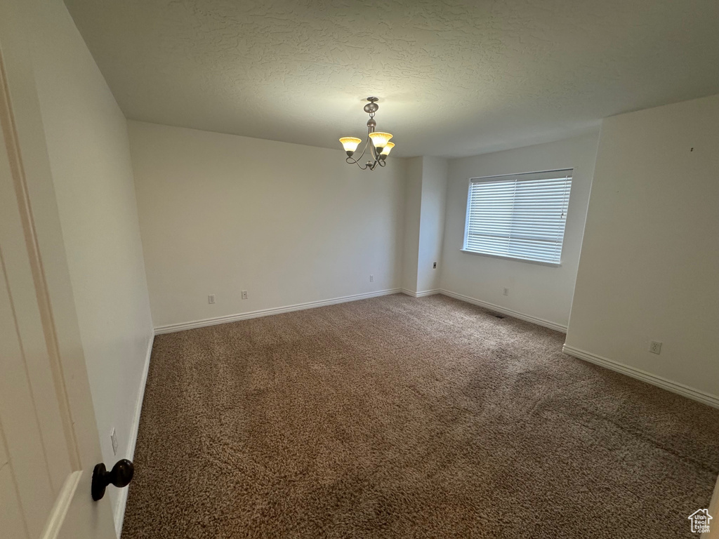Carpeted spare room with a chandelier, a textured ceiling, and baseboards