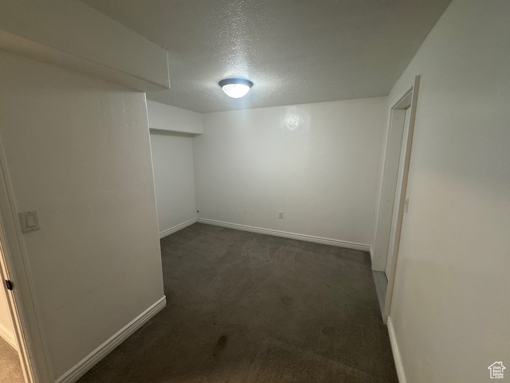 Finished below grade area featuring baseboards, dark colored carpet, and a textured ceiling