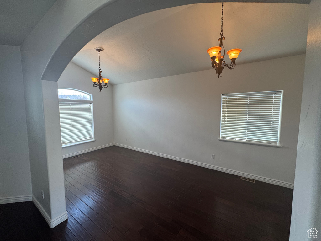Spare room featuring a chandelier, baseboards, dark wood finished floors, and lofted ceiling