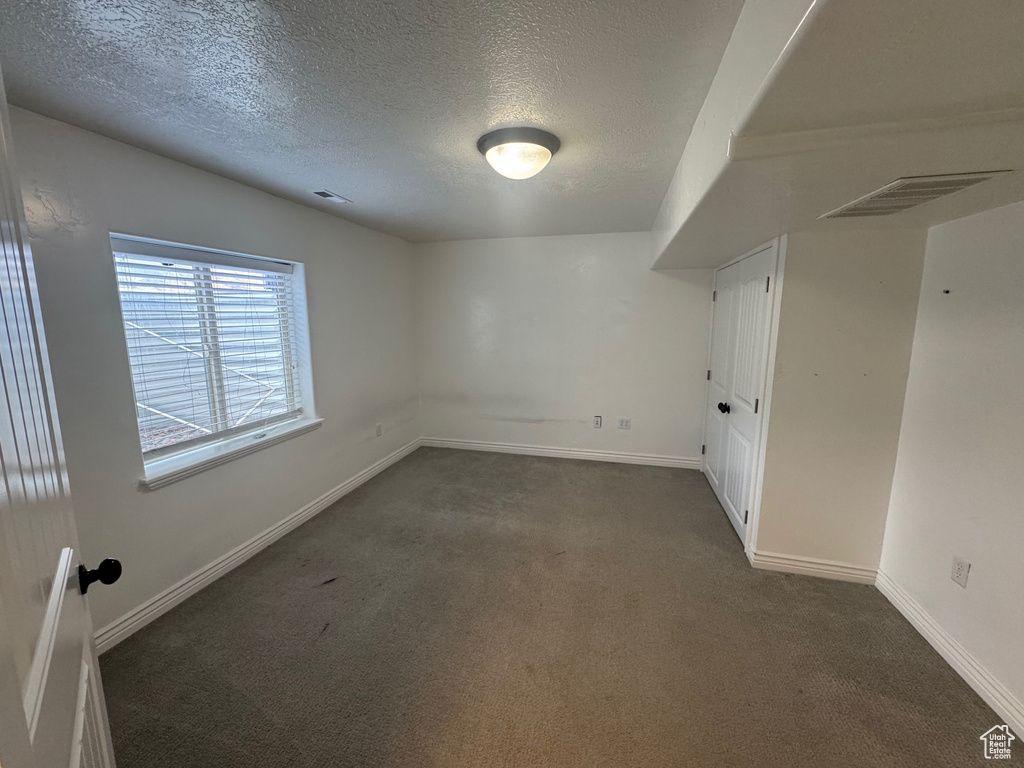 Spare room featuring a textured ceiling, dark carpet, visible vents, and baseboards