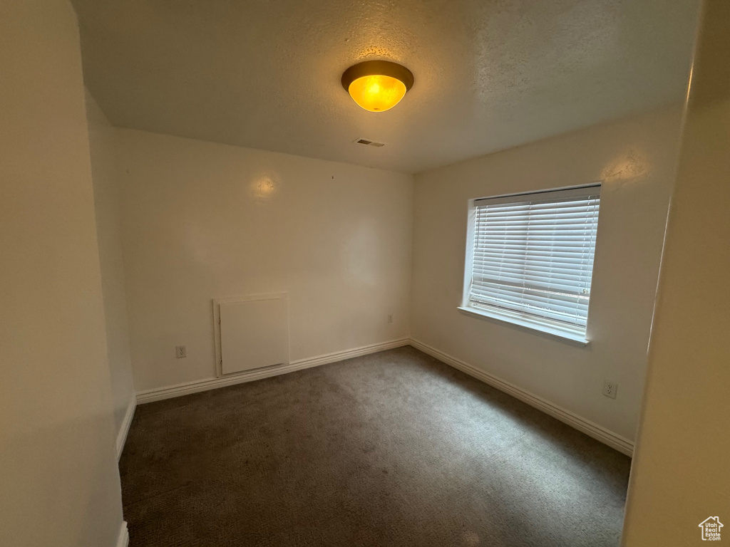 Empty room with dark colored carpet, visible vents, a textured ceiling, and baseboards