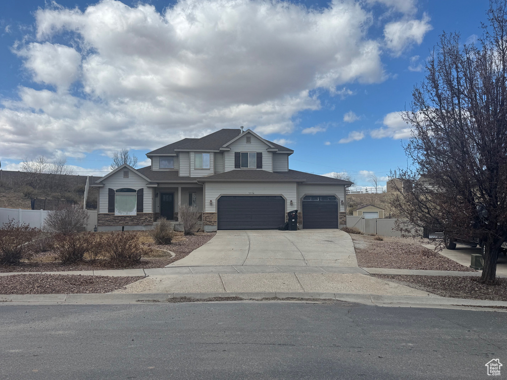 View of front of house with an attached garage, stone siding, fence, and concrete driveway