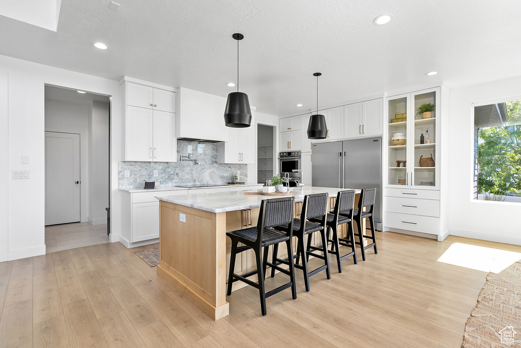Kitchen featuring appliances with stainless steel finishes, backsplash, light wood finished floors, a large island with sink, and recessed lighting