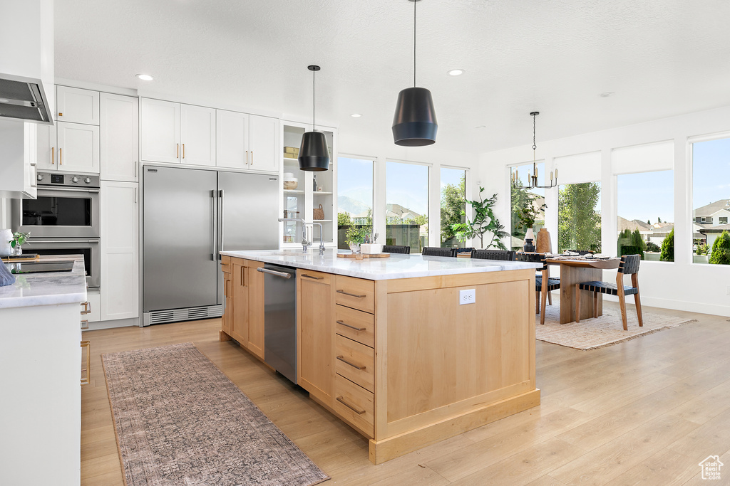 Kitchen with appliances with stainless steel finishes, light wood-style floors, recessed lighting, hanging light fixtures, and light brown cabinetry